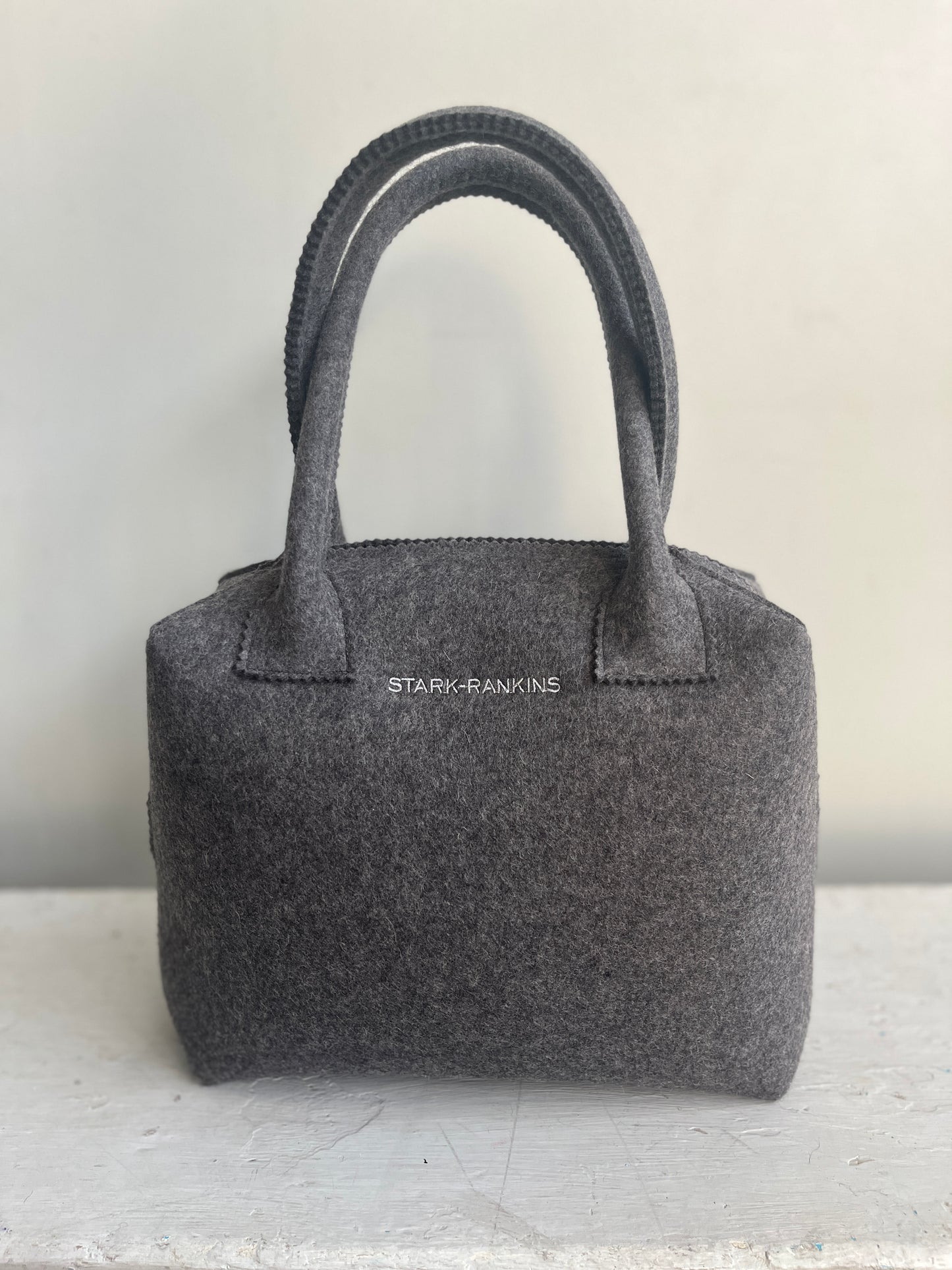 A gray felt handbag with two handles, featuring the text "STARK-RANKINS" on the side, placed against a neutral background.