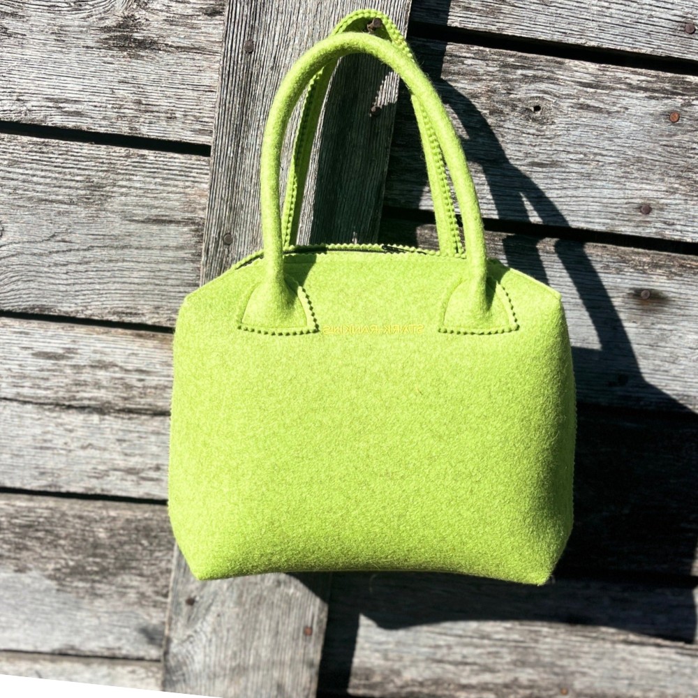 A bright green felt handbag with two handles hangs on a wooden fence.