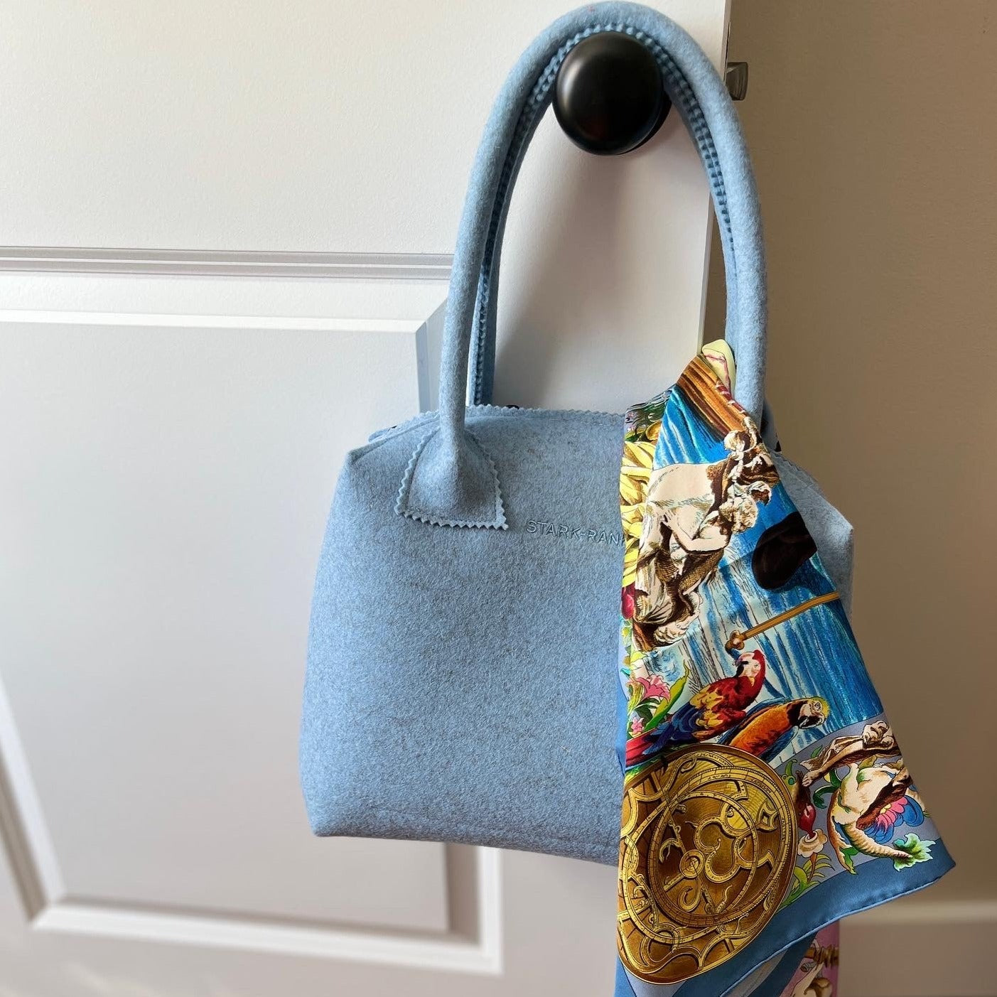 Light blue handbag hanging on a doorknob, adorned with a colorful patterned scarf.