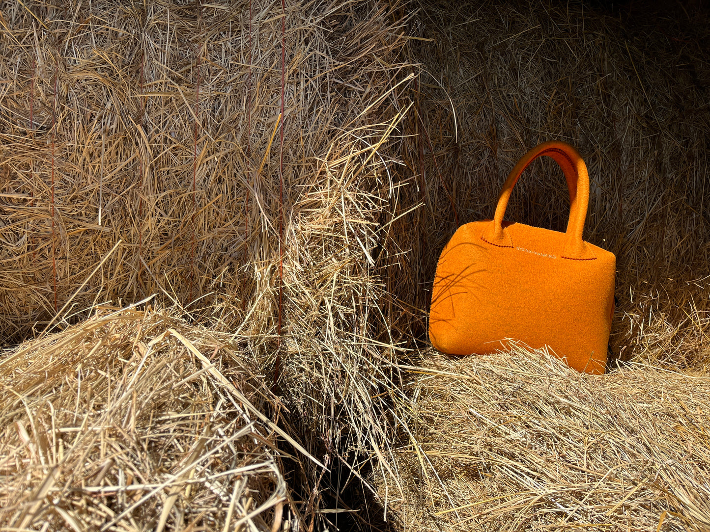 An orange handbag sits on a stack of hay bales.