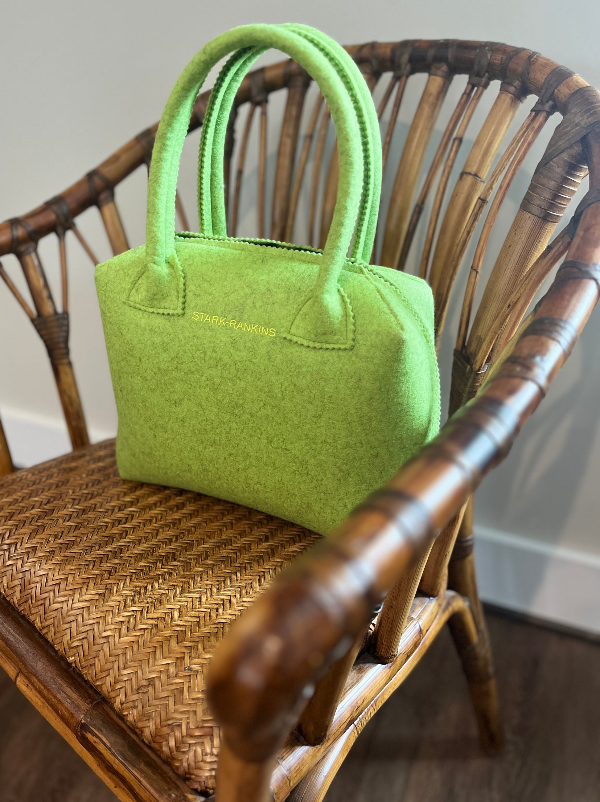 A green handbag sits on a woven wooden chair.