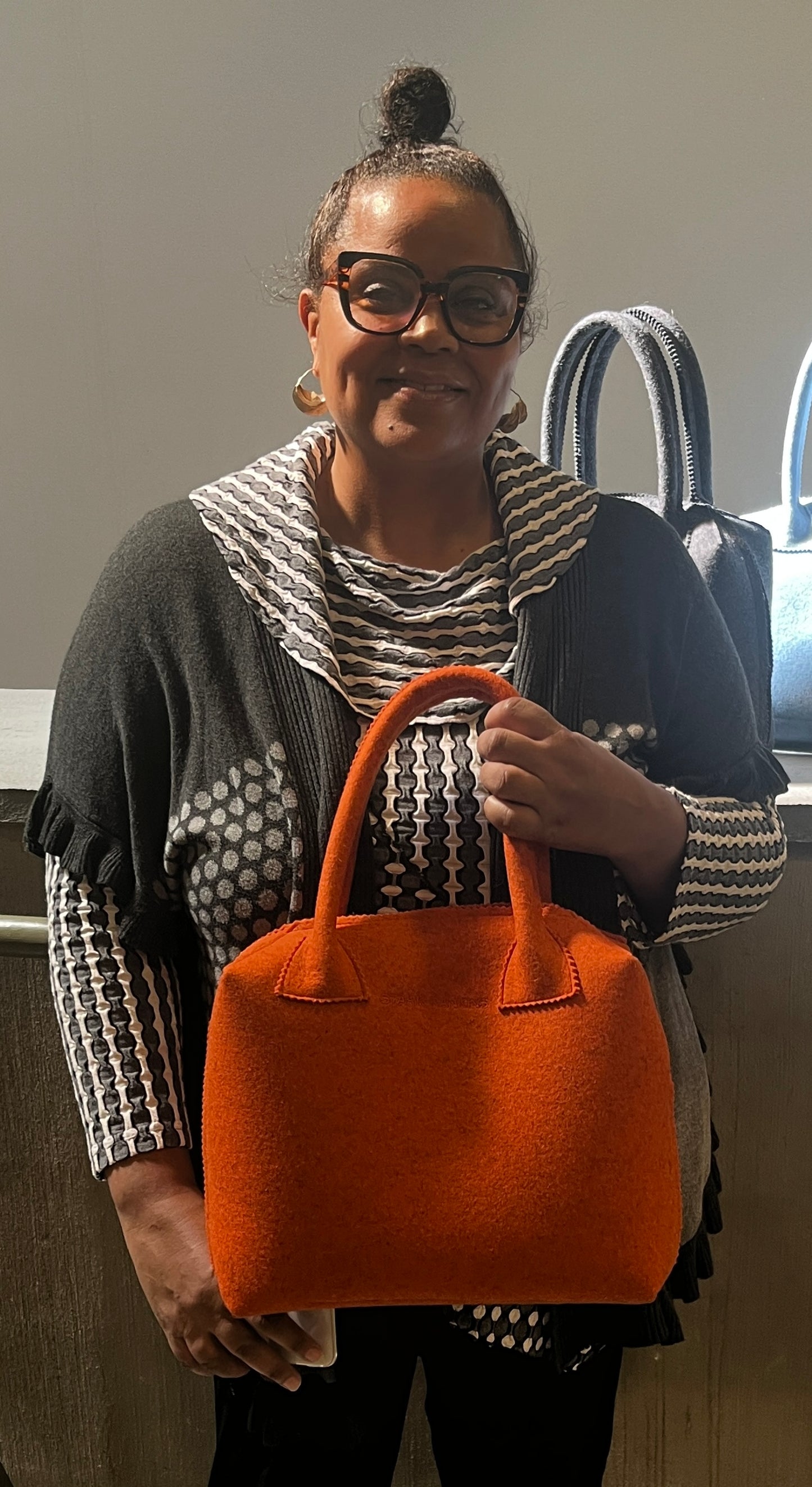 Person holding an orange handbag, wearing glasses and a patterned sweater.