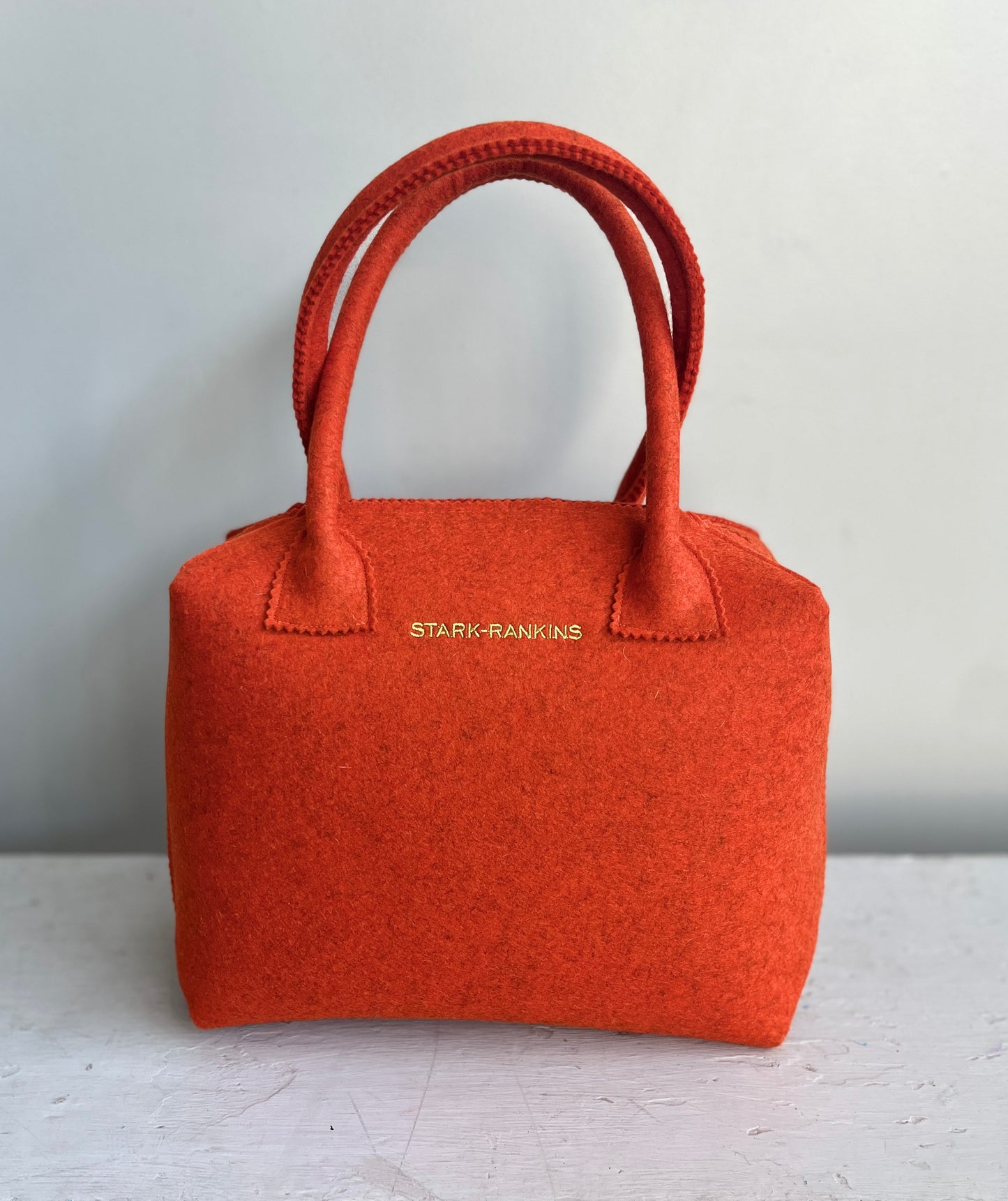 A bright orange handbag with two handles and the brand name "STARK-RANKINS" printed in gold on the front.