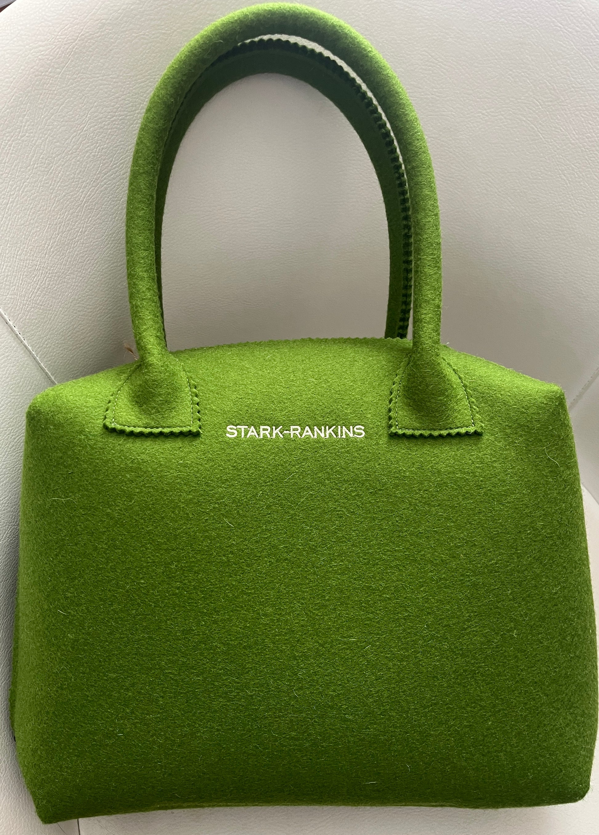 A green felt handbag with "STARK-RANKINS" written in white on the front, placed on a light-colored surface.