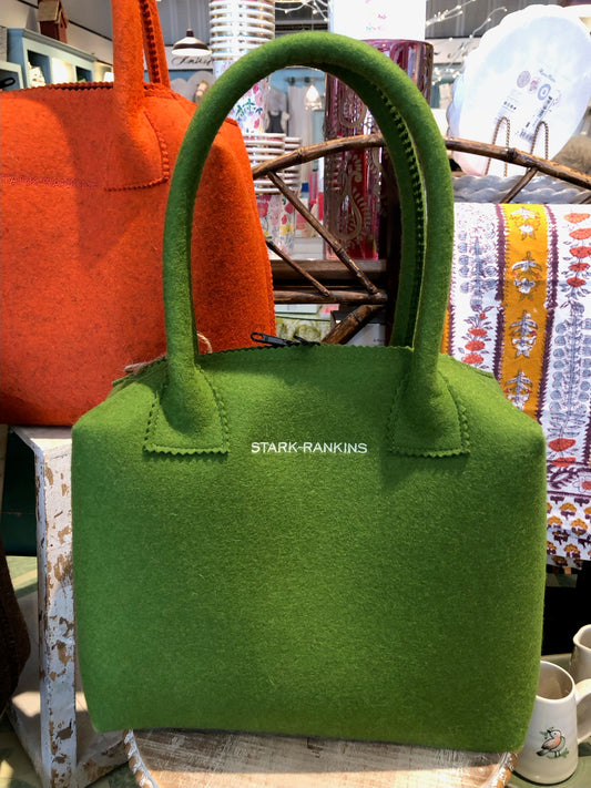 A green felt handbag with large handles displayed in a store setting.