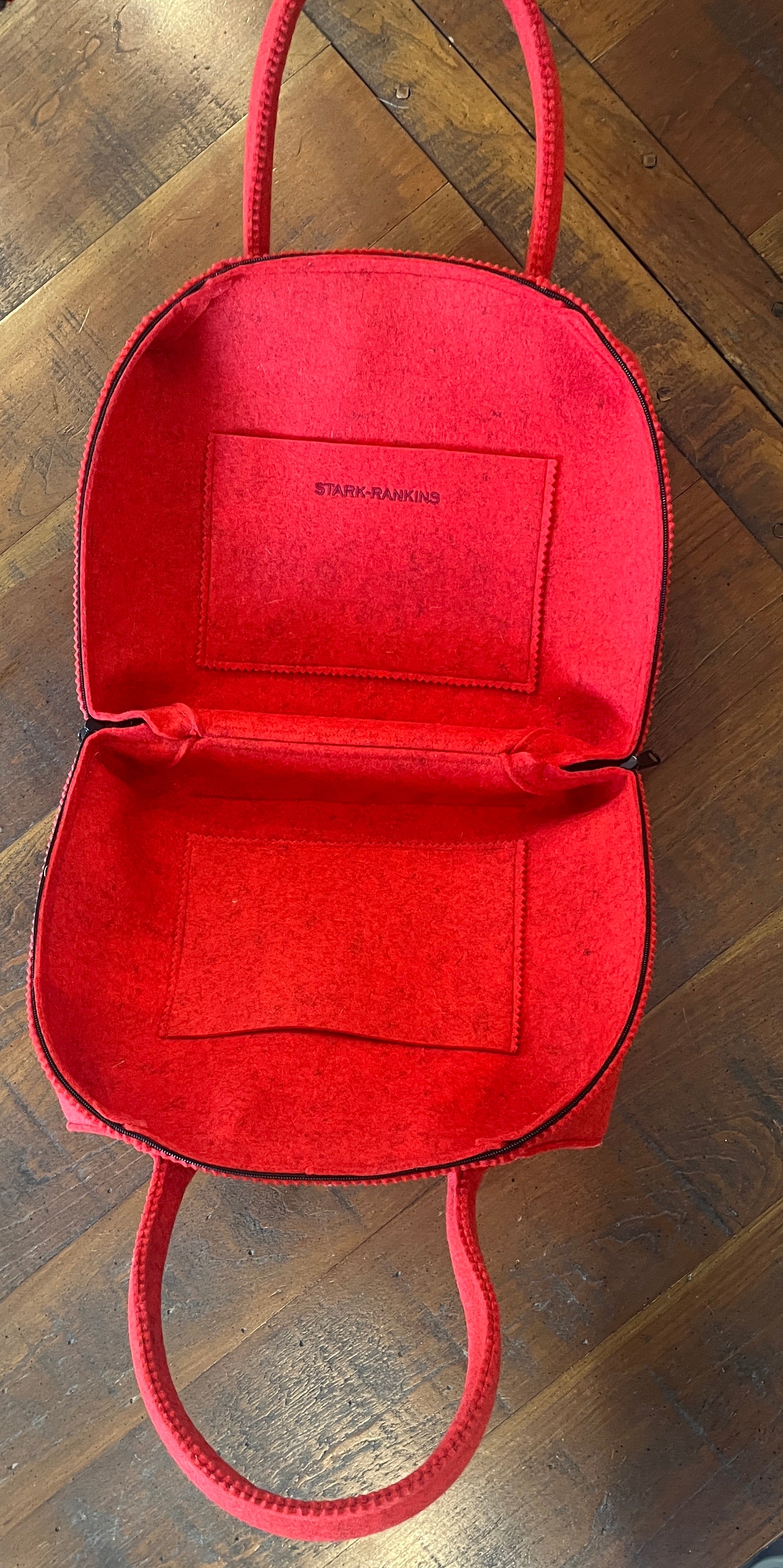 Open red handbag on a wooden surface, displaying an empty interior and a small pocket with "Stark Banking" inscribed inside.