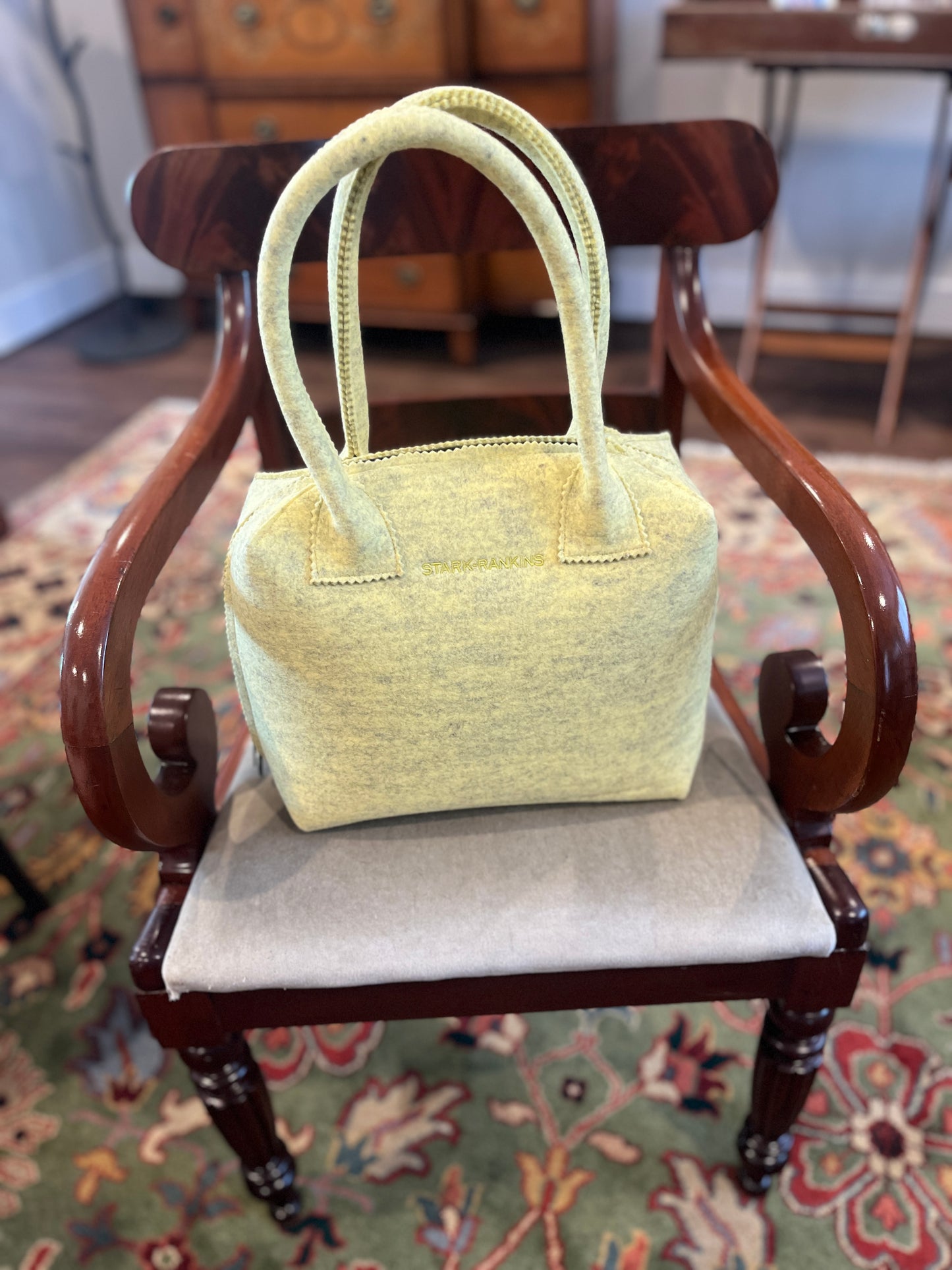 A yellow handbag is placed on a cushioned wooden chair with a patterned rug underneath.